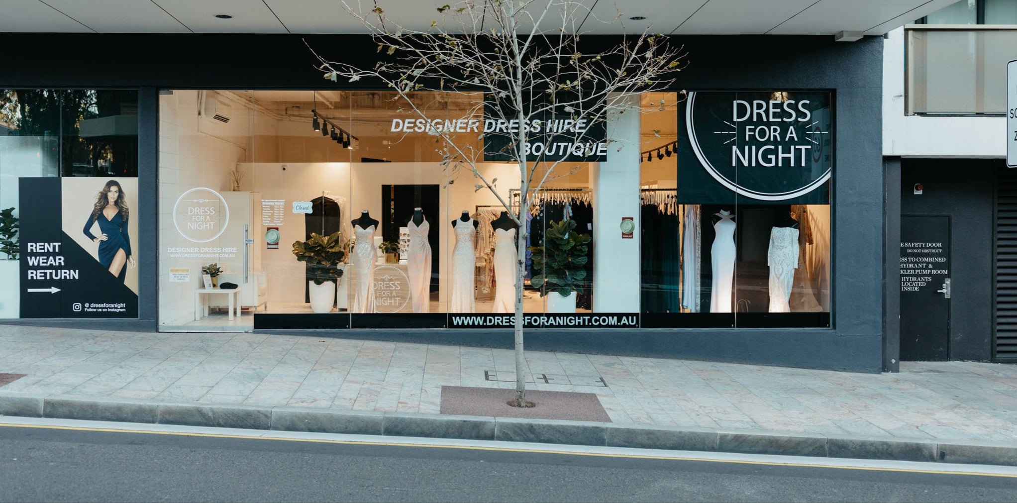 Storefront with a display of dresses and promotional signs for 'Dress for a Night' boutique.